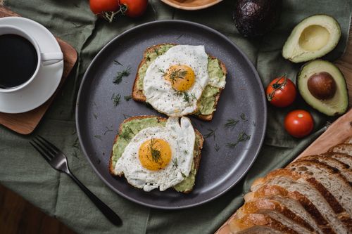 Free Tasty avocado toast topped with sunny side up eggs, served with a cup of coffee. Stock Photo