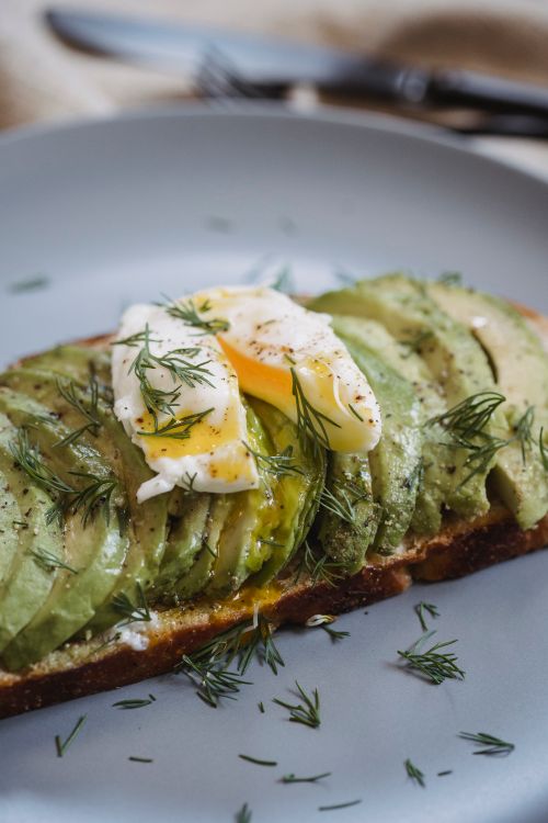 Free Mouthwatering avocado and poached egg toast garnished with dill, perfect for breakfast. Stock Photo