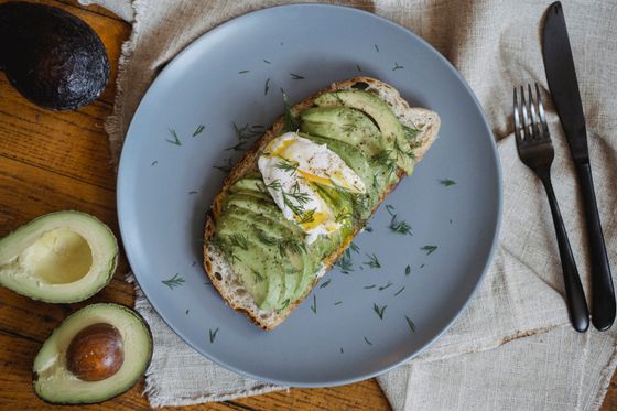 Sourdough toast with fanned avocado slices, poached egg and fresh dill on a blue plate