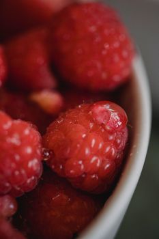 Close-up shot of fresh, juicy raspberries in a white bowl, showcasing vibrant red color and texture.