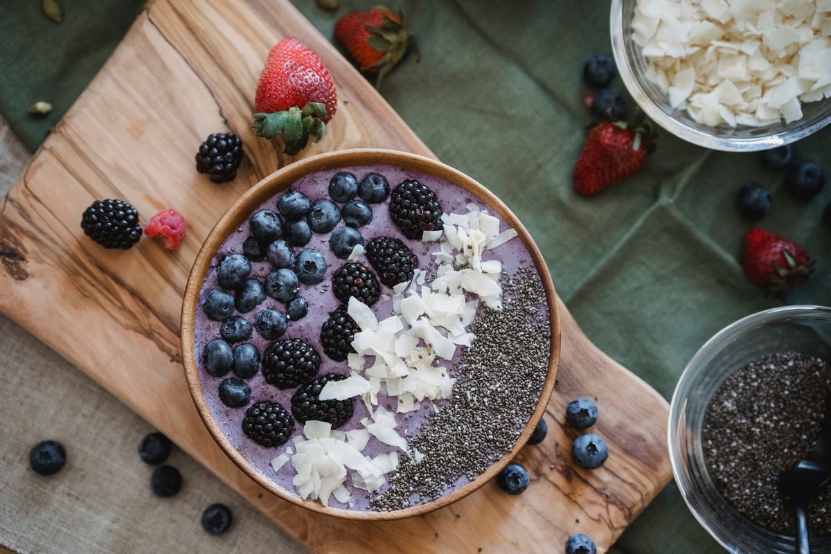 Purple smoothie bowl topped with blueberries, blackberries, coconut chips and chia seeds on a board