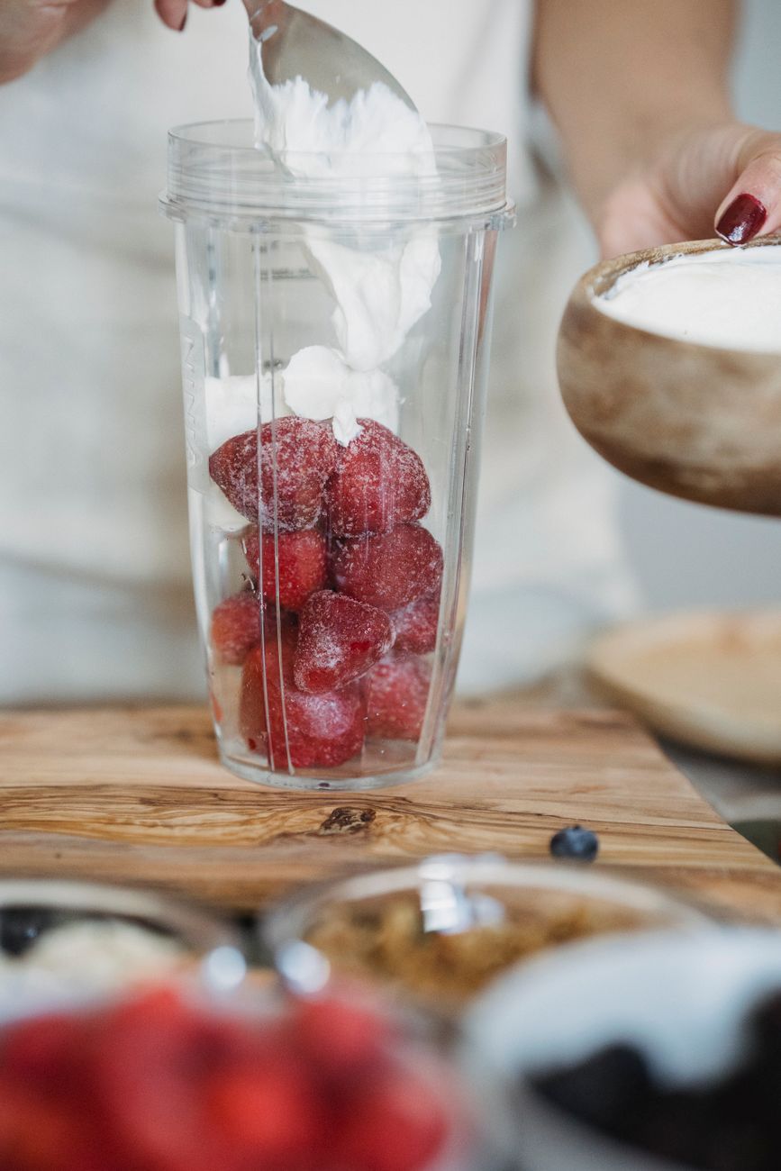 Close view of strawberries and yoghurt being added to a blender for a morning smoothie.