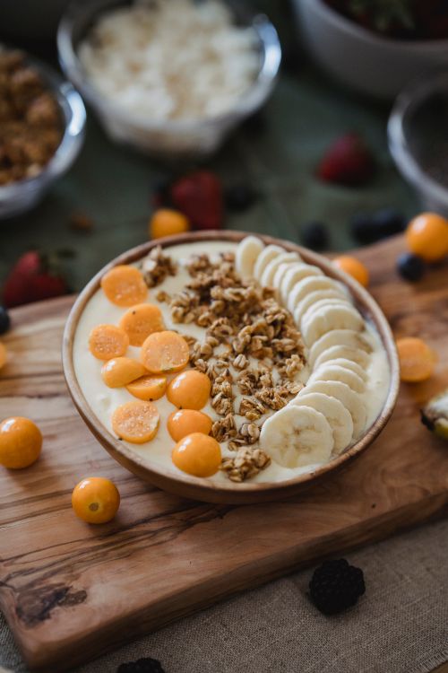 Free Delicious granola and fruit breakfast bowl with bananas and cape gooseberries on a wooden board. Stock Photo