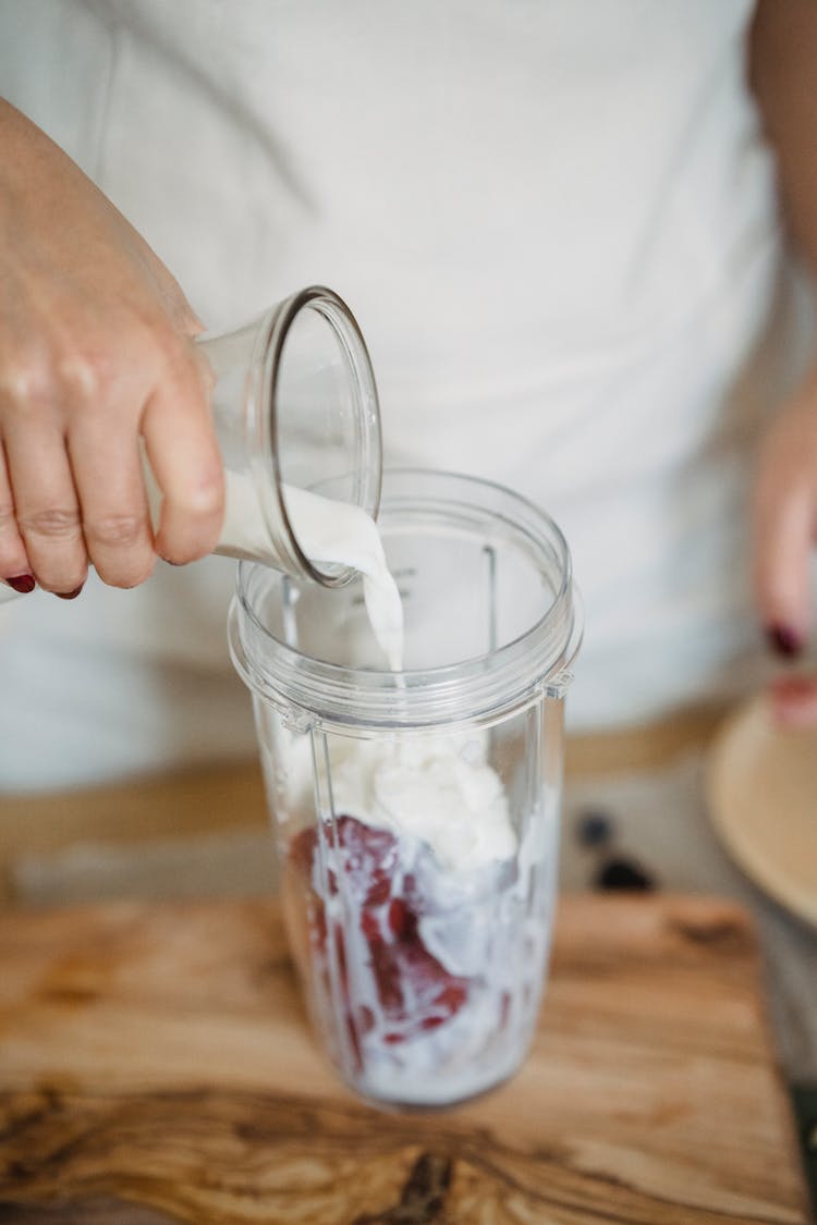 A Hand Pouring Milk On A Clear Container