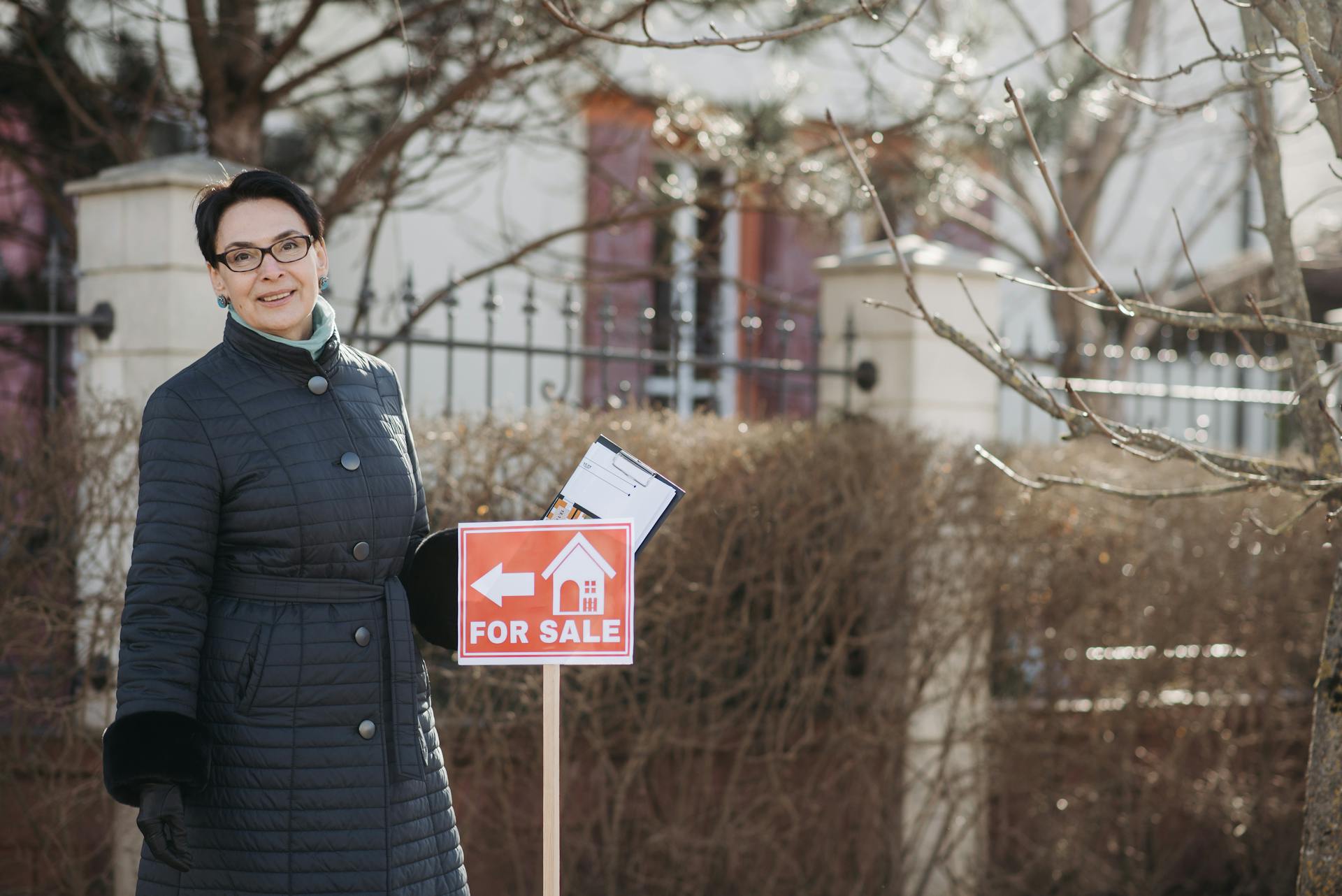 Smiling Realtor Standing by a For Sale Sign