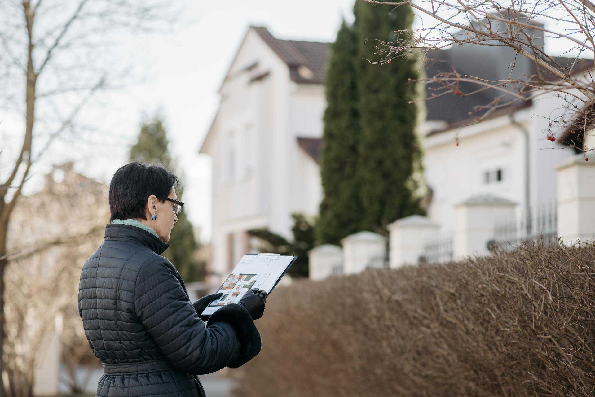 Realtor assessing house with clipboard during winter season outdoors. Ideal image for real estate content.