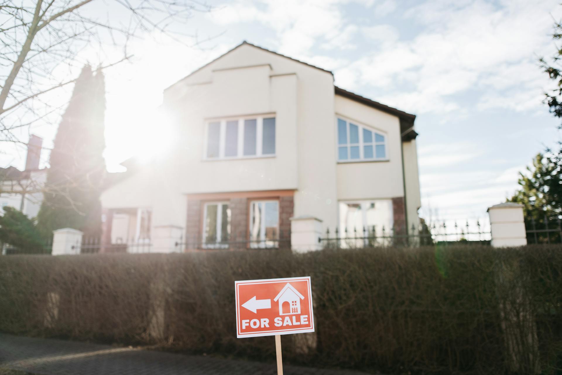 Bright suburban house exterior with a for sale sign in the foreground.