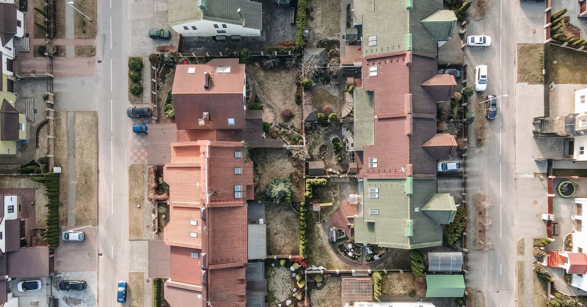 Aerial drone shot of a residential area with houses, streets, and parked cars.