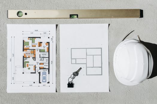Blueprints, spirit level, and hard hat symbolize house planning.