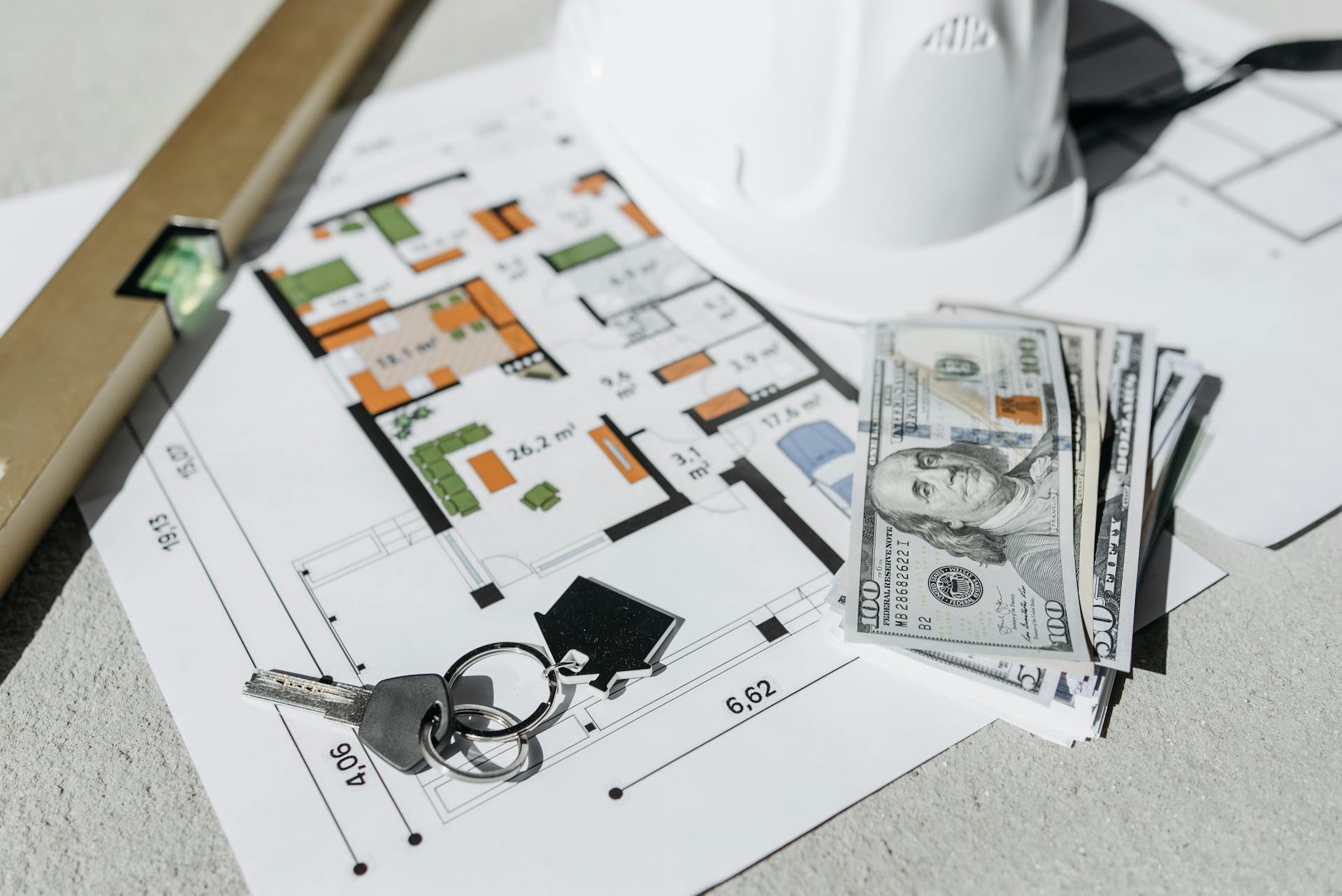 Floor plan with cash, keys, and hard hat symbolizing real estate investment and property planning.