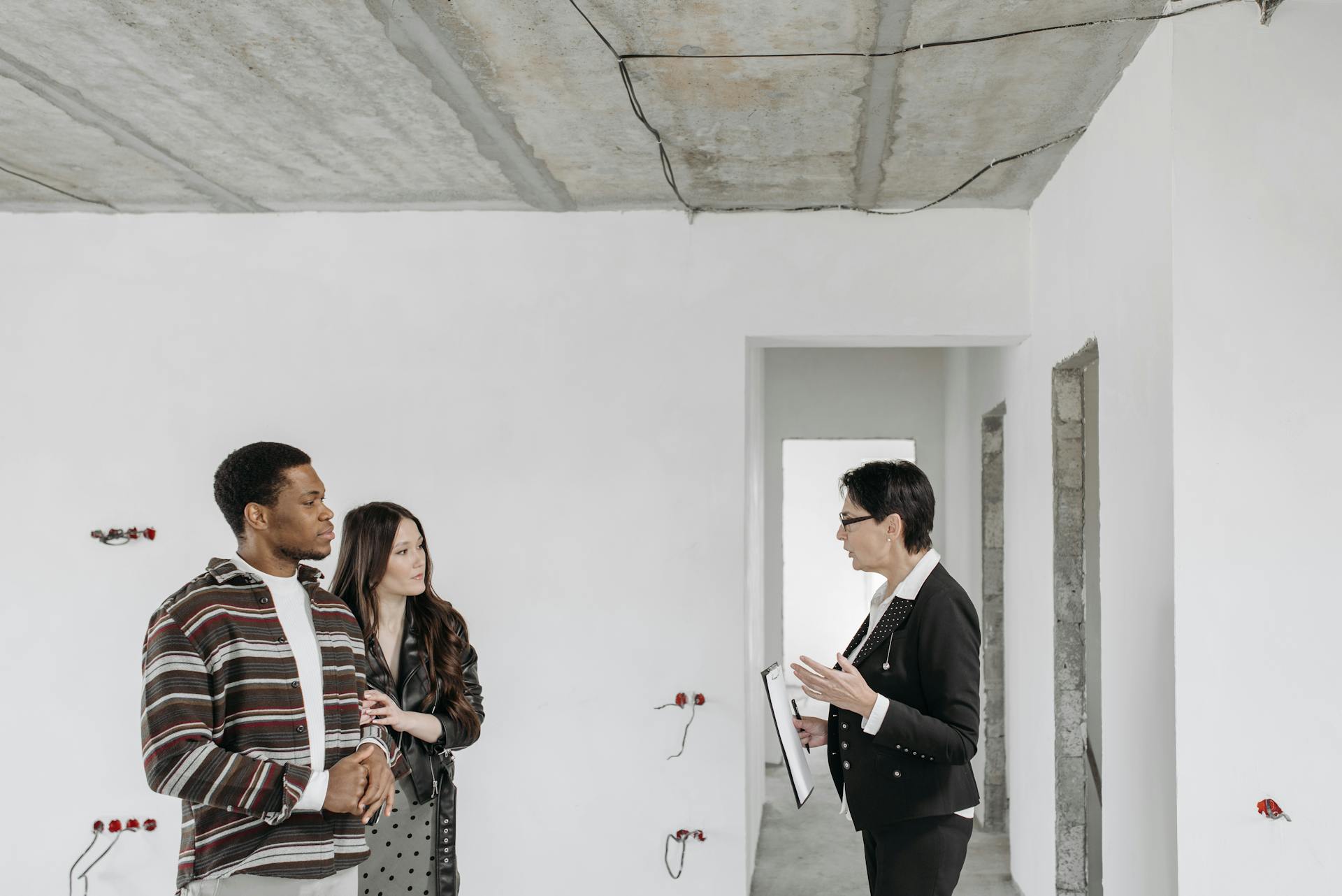 Real estate agent discussing property details with clients in an unfinished apartment.