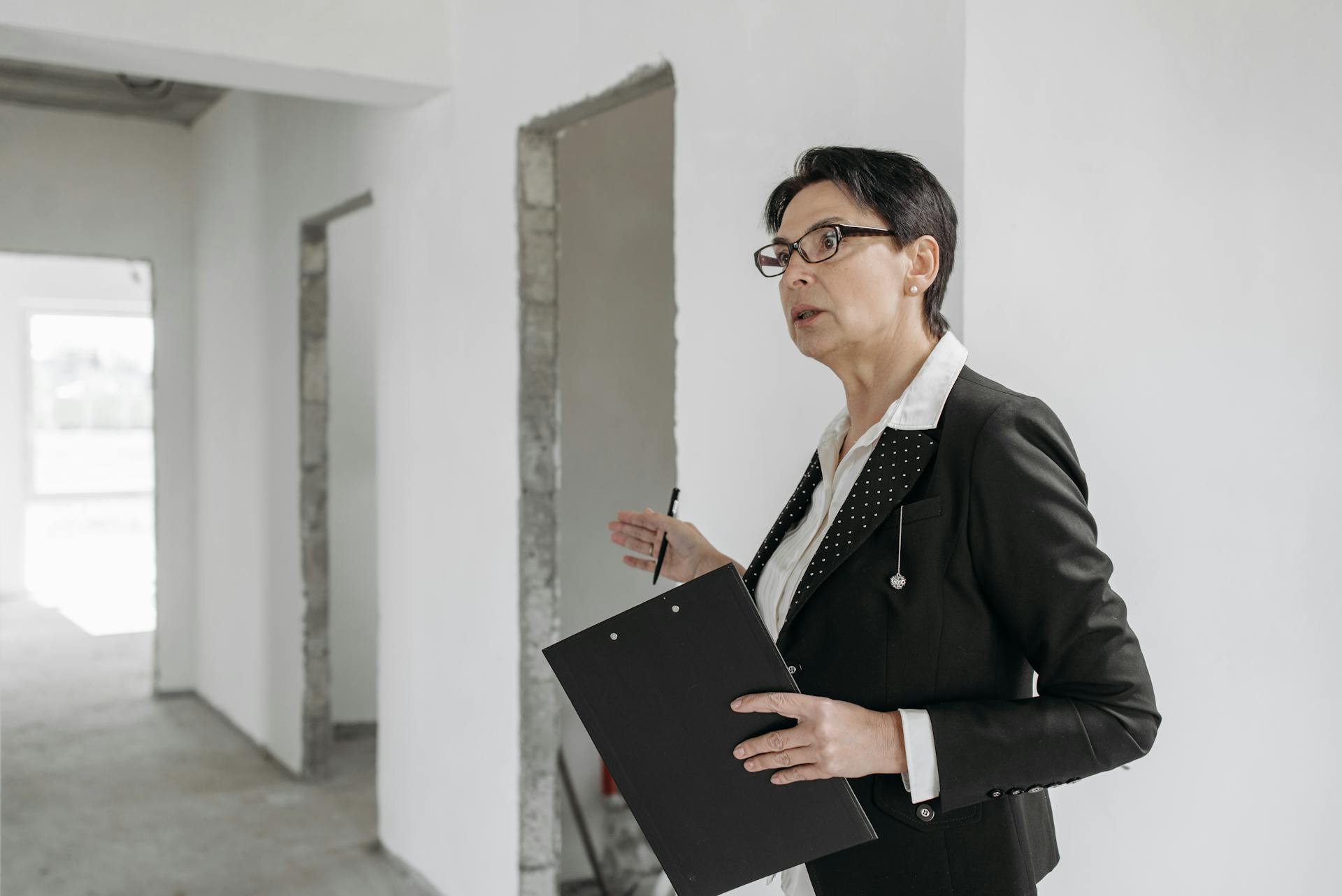 Woman in a suit holding a clipboard, inspecting an unfinished indoor construction site.