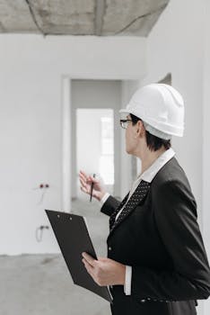A professional engineer in a suit and hard hat inspecting a construction site with a clipboard.