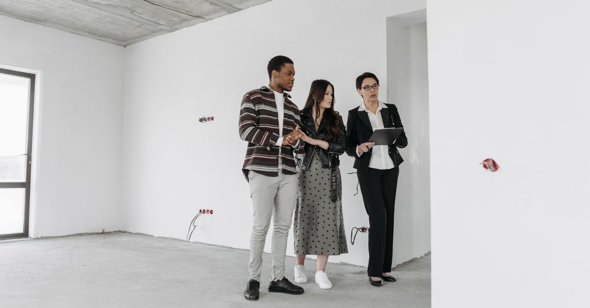 Real estate agent with clients exploring an unfinished apartment interior.