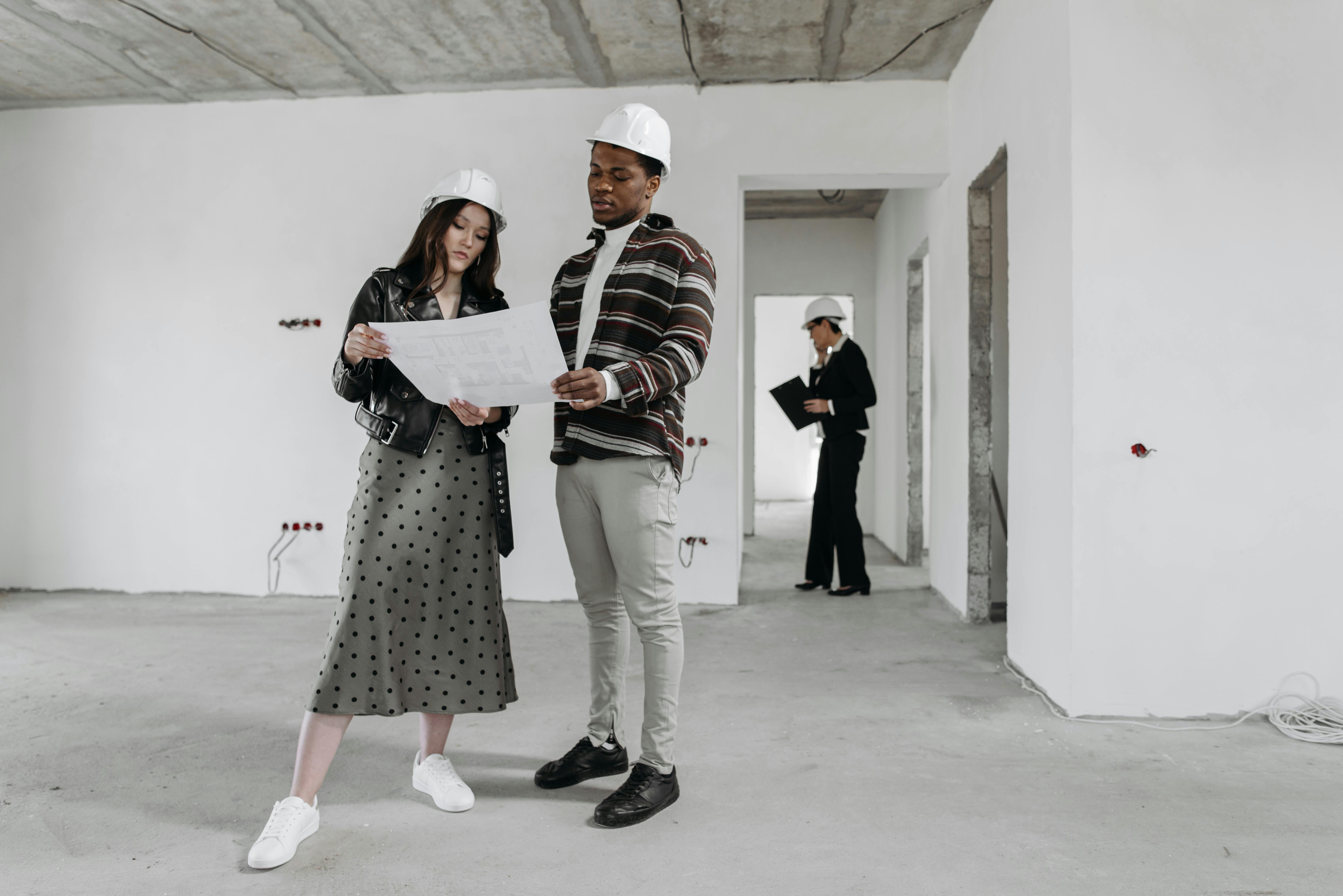 Two architects examine blueprints in a partially finished building while discussing design plans.