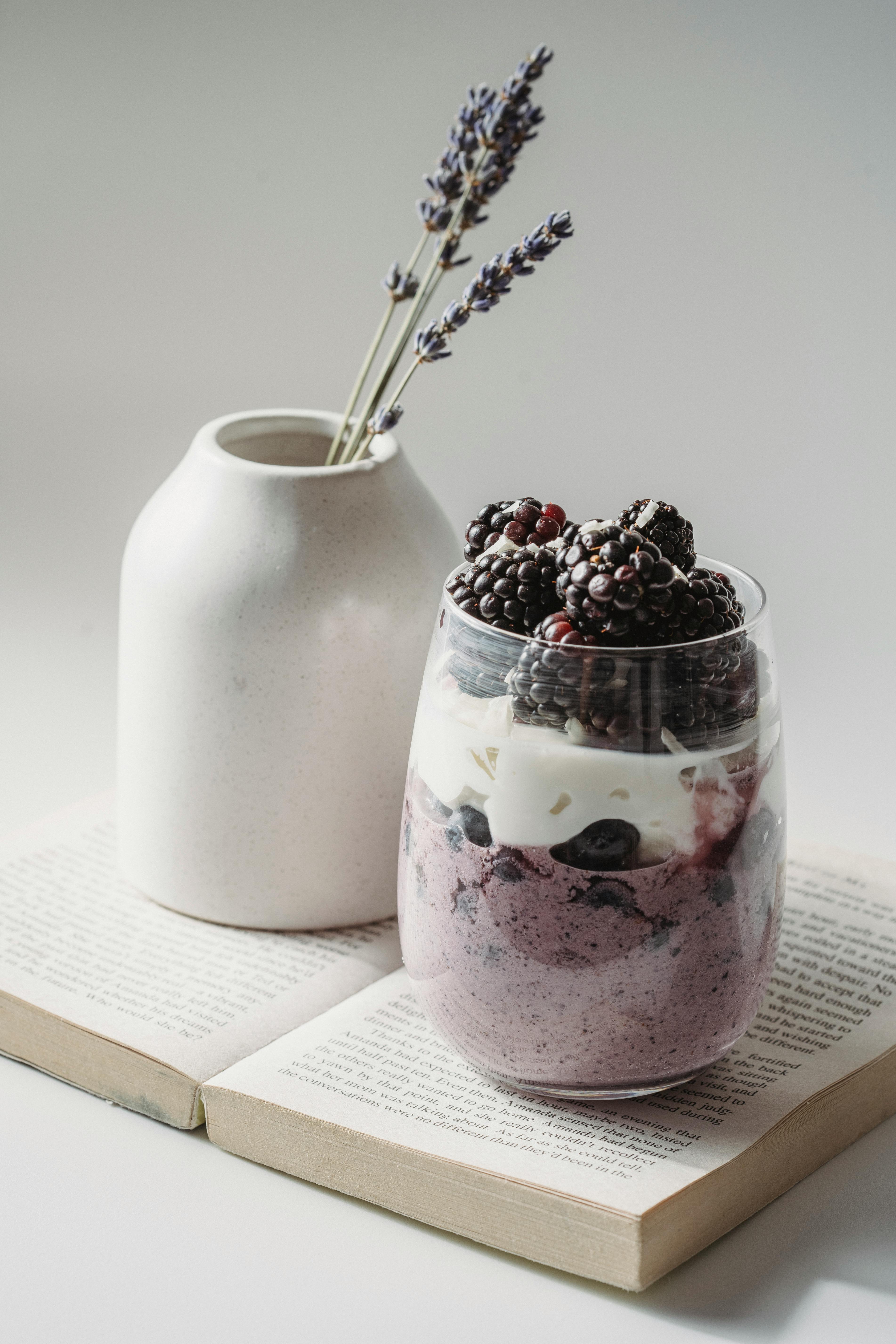 glass with yogurt and fruit and a vase with lavender on a book