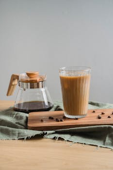 Refreshing iced coffee in a glass, served with coffee pot on a rustic tray.