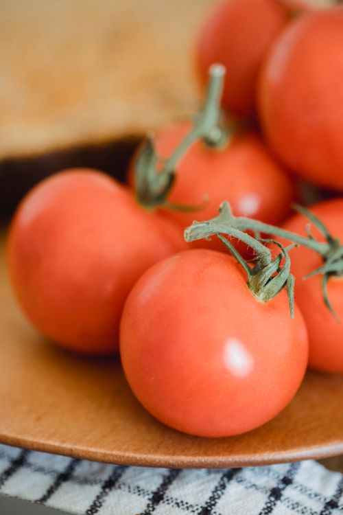 Free Fresh tomatoes on a wooden plate, highlighting their vibrant color and healthy appeal. Stock Photo