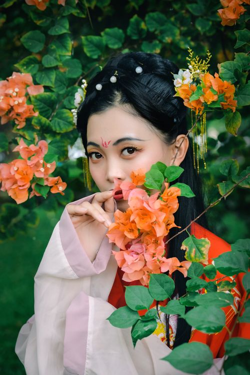 Free Portrait of an Asian woman in traditional attire framed by vibrant bougainvillea flowers outdoors. Stock Photo
