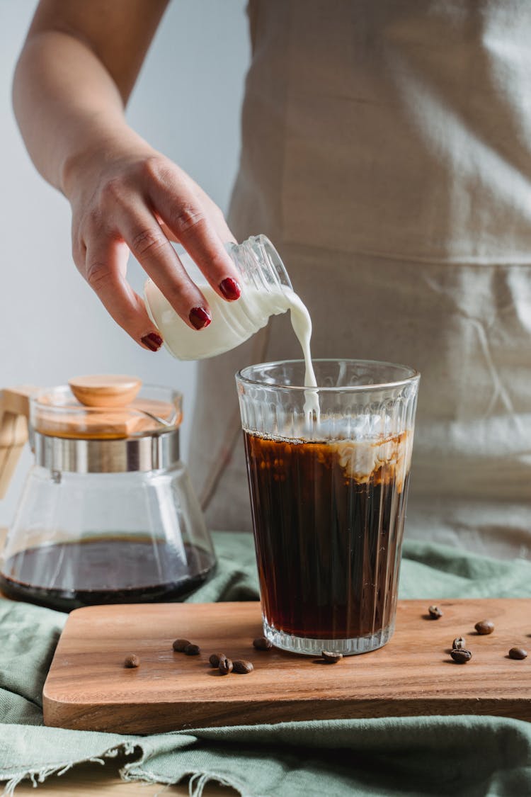 Woman Pouring Milk Into Coffee In A Glass