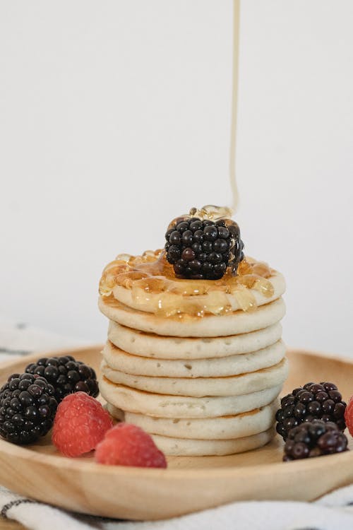 Free Pouring Honey on Pancakes with Berries on Wooden Plate Stock Photo