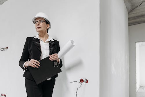 Woman in Black Suit and White Helmet Holding White Paper Beside White Wall