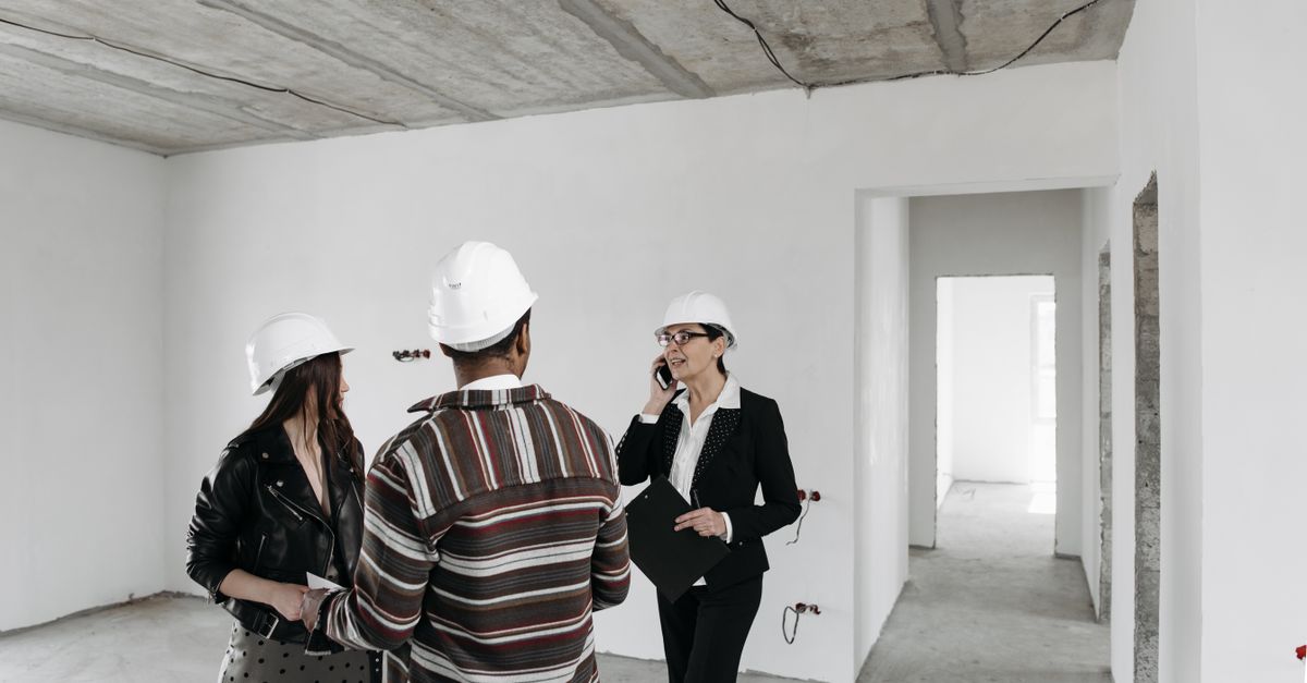 Agente inmobiliario explicando detalles de una reforma a una pareja en una vivienda en obras