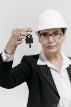 Confident female real estate agent in a hard hat holding a house key, symbolizing property acquisition.