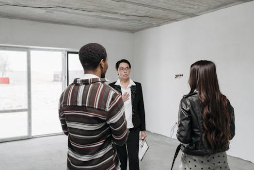 Realtor showing young couple a house, discussing details inside a modern, unfurnished space.