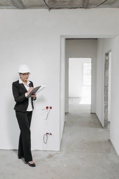 A Woman Wearing Hard Hat Writing on a Document she is Holding