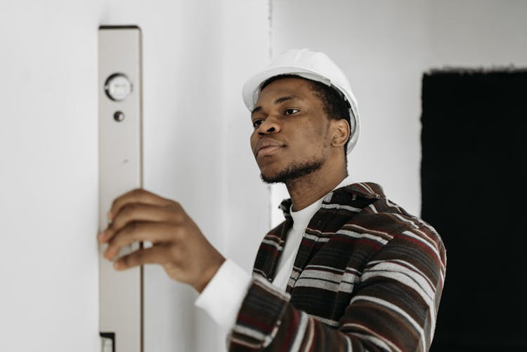 Man In Striped Shirt With White Hard Hat Holding A Level Tool