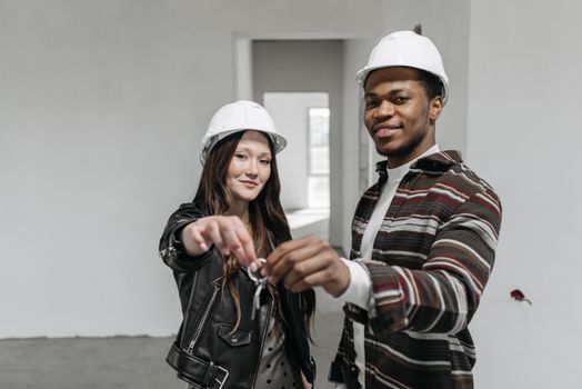 A happy couple holding keys in a newly bought house, wearing white helmets.