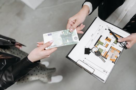Close-up of a real estate transaction with euro bill, keys, and floor plan.