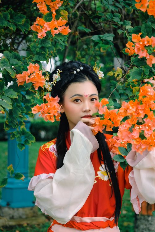 Free Elegant portrait of a woman in traditional Asian attire surrounded by vibrant flowers outdoors. Stock Photo