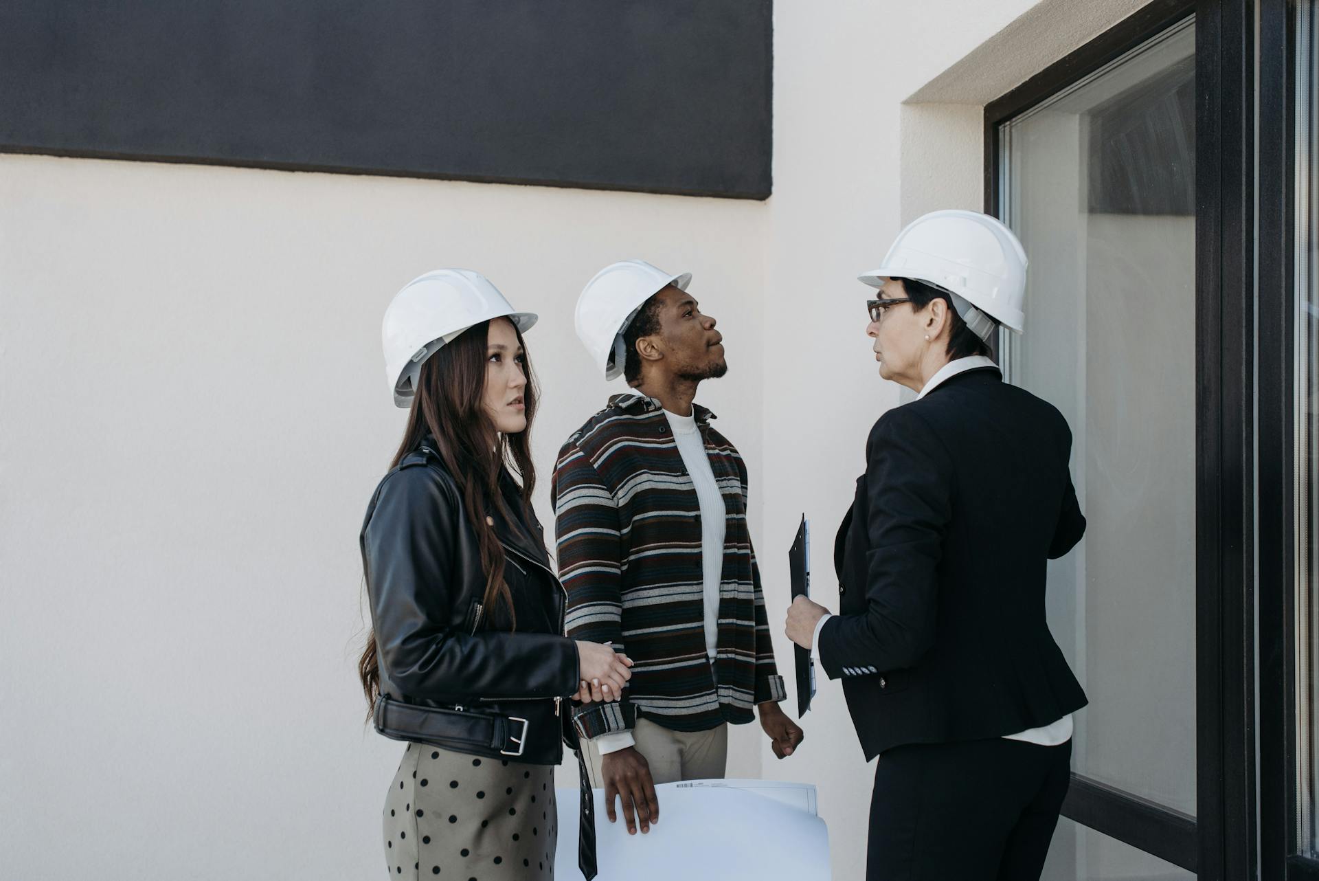 A diverse group of professionals in construction helmets reviewing property plans outdoors.