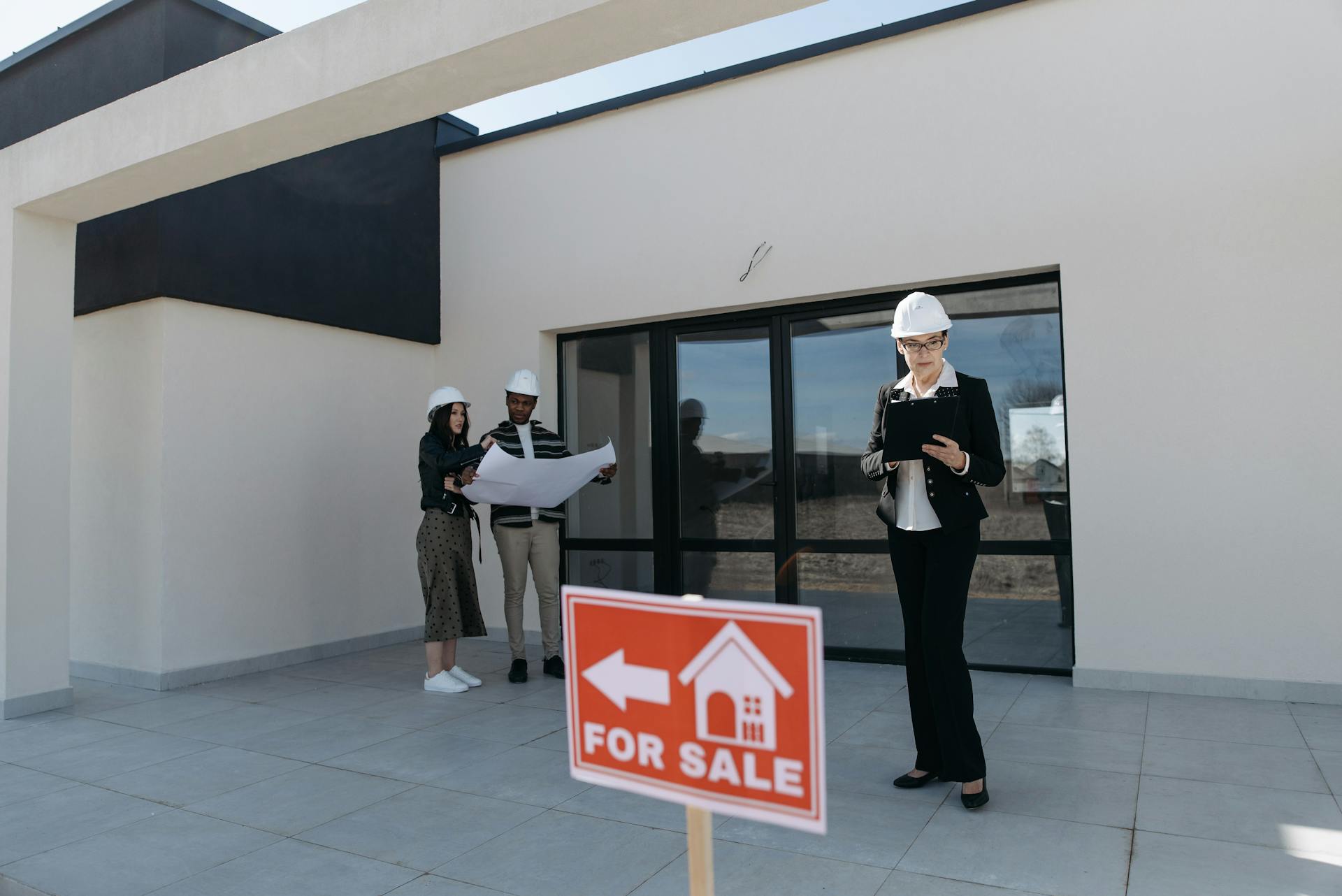 Real estate agents in hard hats reviewing plans beside a house for sale.