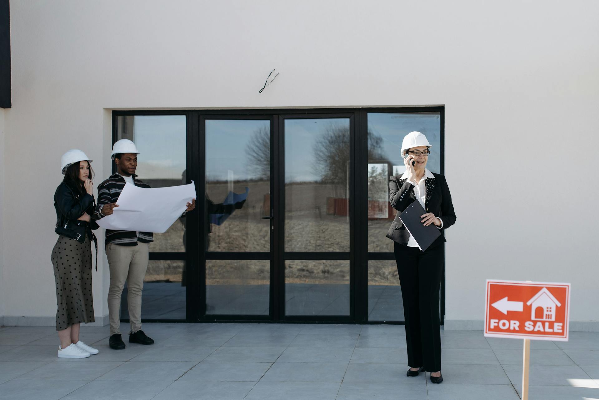 Real estate professionals with hard hats inspect a property for sale. Outdoor meeting with blueprints.