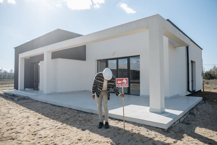 A Man Posting A For Sale Sign Near A House