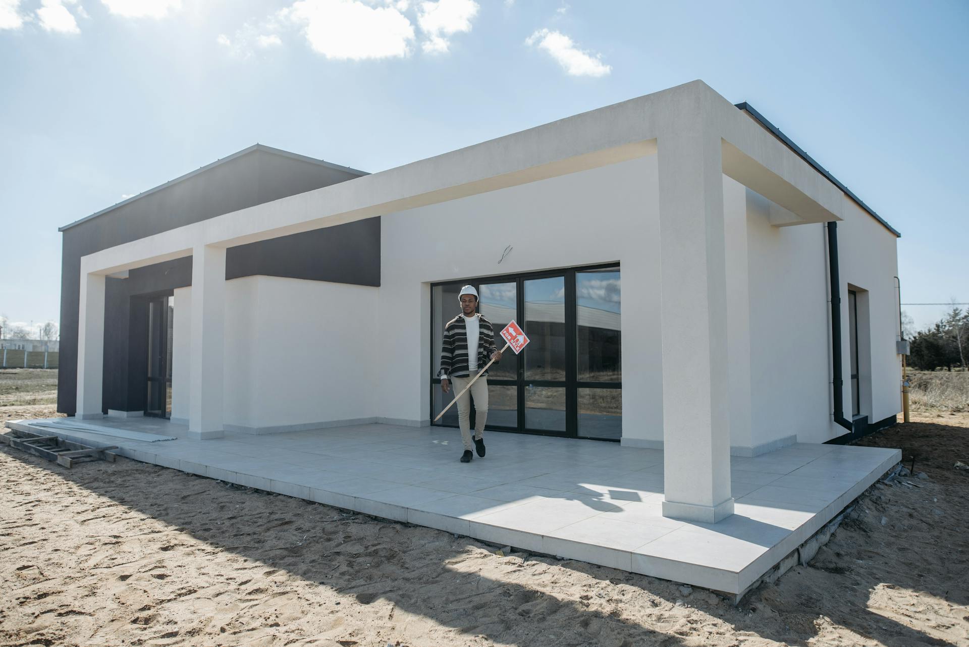 Real estate agent holding a for sale sign in front of a new modern house.