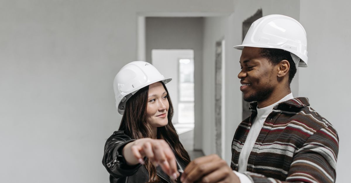 A smiling couple wearing safety helmets, holding keys, symbolizing new home ownership.