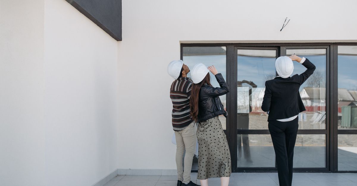 Three architects evaluating exterior building structure, wearing helmets and business attire.