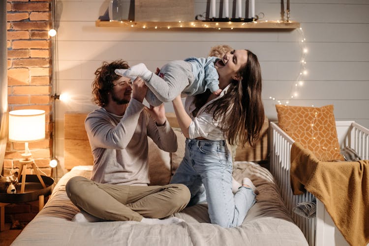 A Man And A Woman Playing With A Child In The Bedroom