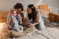 Woman in White Long Sleeve Shirt Sitting on Bed Beside Girl in Gray Sweater