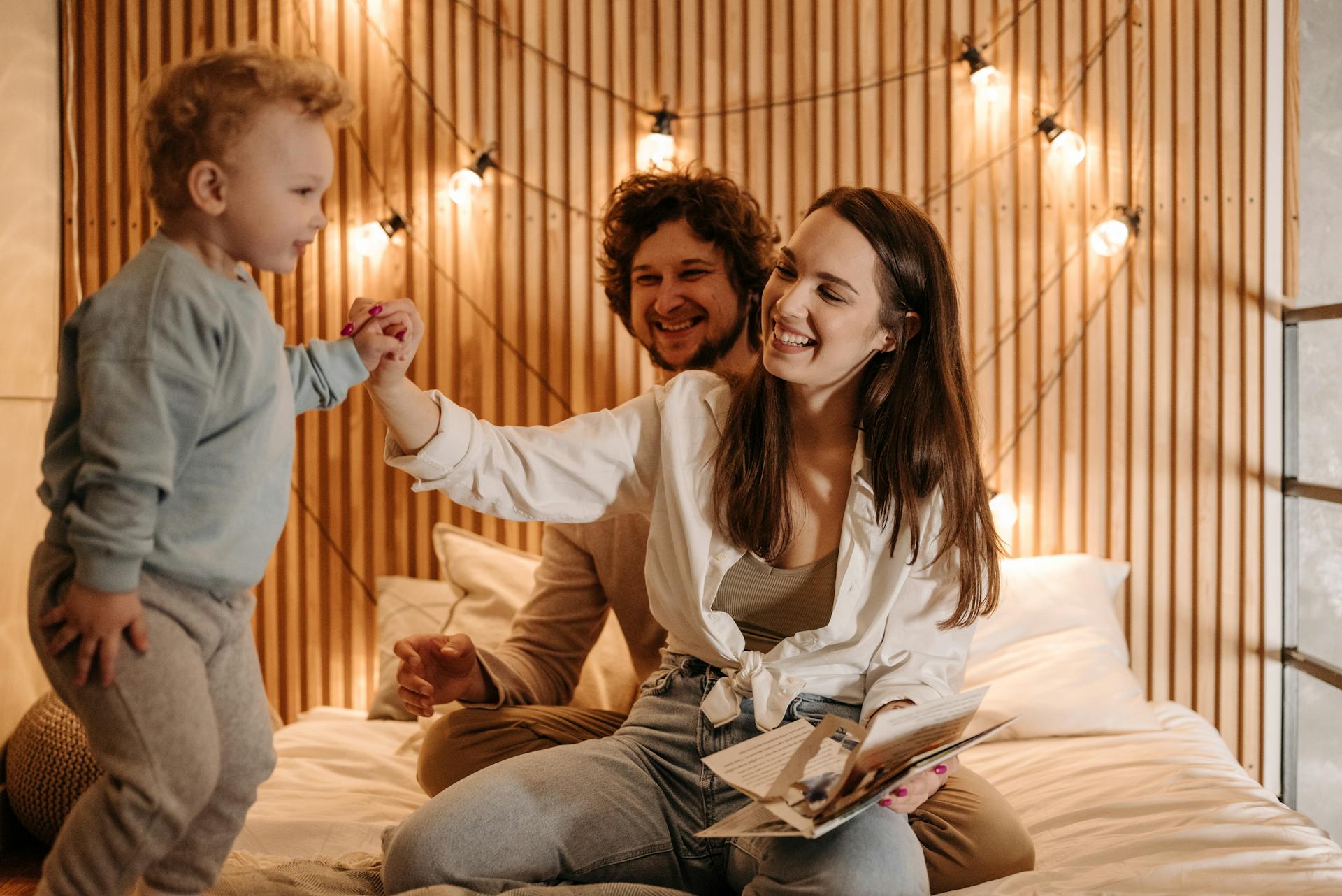 Une joyeuse journée en famille, dans un lit confortable, avec des parents souriants et un enfant enjoué.