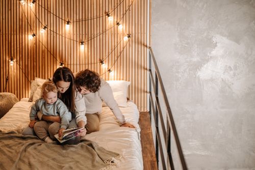 Free Family bonding over a storybook in a warmly lit, cozy bedroom. Ideal for lifestyle and family themes. Stock Photo