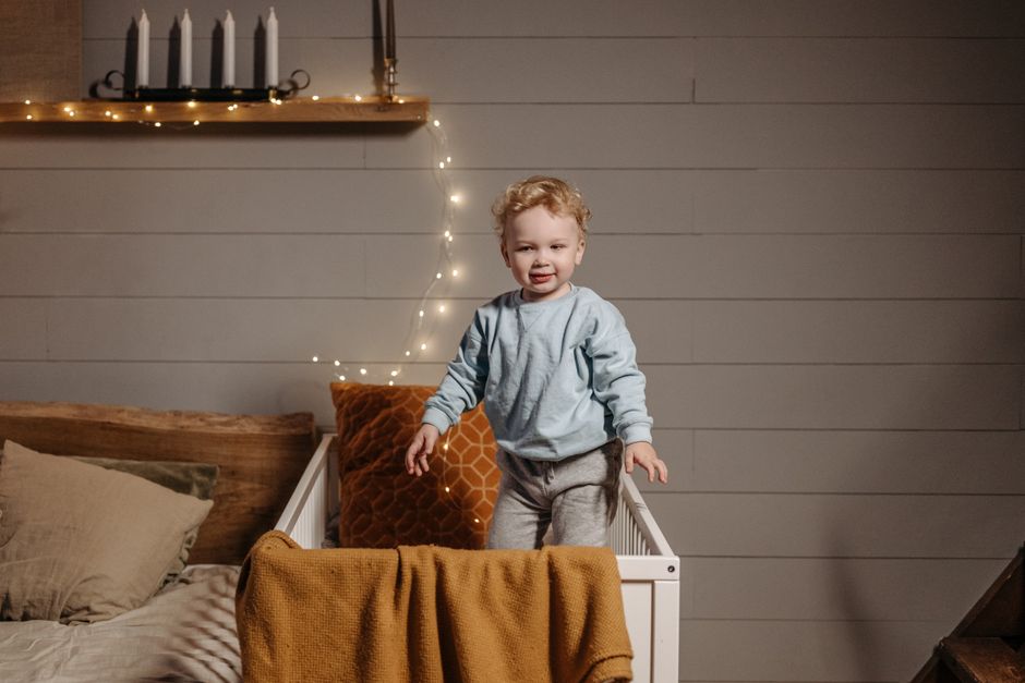 What Safety Research Reveals About Cribs, Monitors, and Sleep Gear A cute baby standing in a crib with cozy decor and fairy lights in a bedroom.