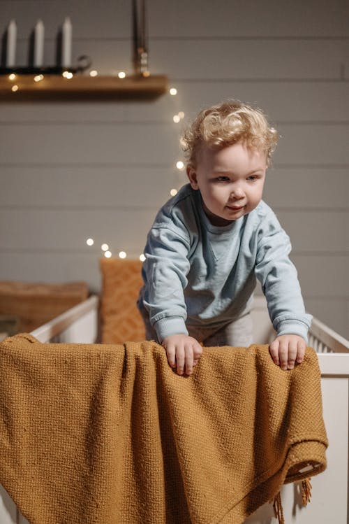 Free A Cute Baby in Light Blue Sweater Standing at the Crib Stock Photo