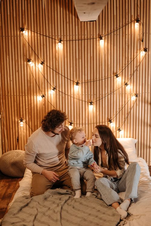Free Family bonding in a cozy, warmly lit room with string lights on a wooden wall backdrop. Stock Photo