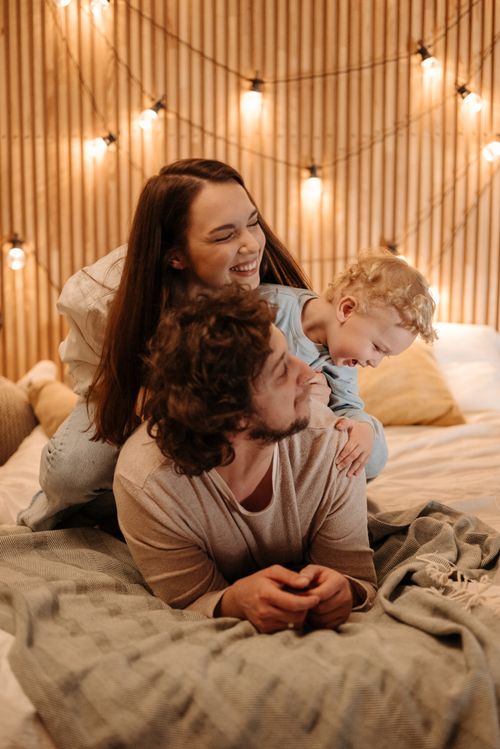 Free A cheerful family enjoys bonding time together on a bed with warm lighting. Stock Photo