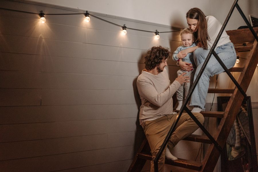 A loving family moment captured as parents help their toddler on stairs indoors.